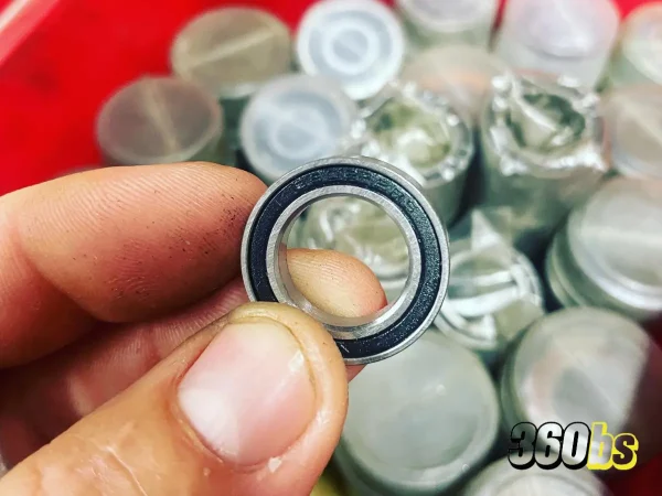 Mano sosteniendo un rodamiento de bicicleta BMX, con un fondo desenfocado de más rodamientos envasados.