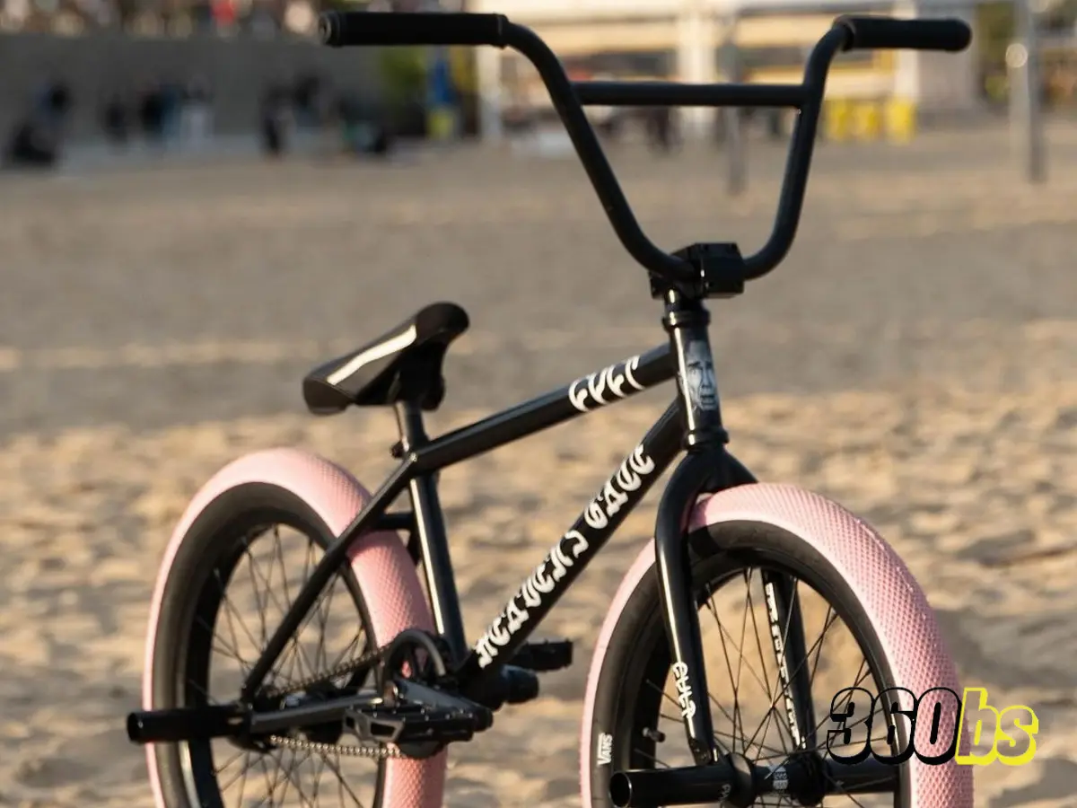 Bicicleta BMX negra con neumáticos rosados estacionada en la playa