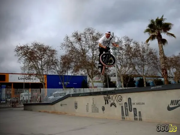 Rider BMX realizando salto en entorno urbano con cielo nublado